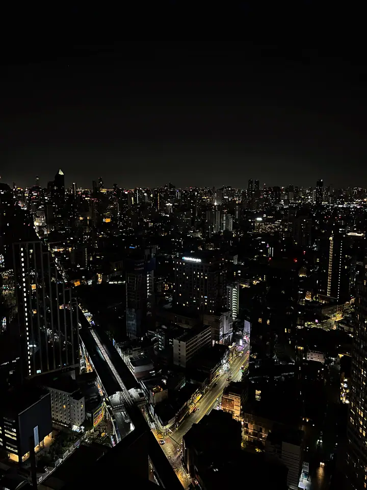 Night skyline over Bangkok with roads cutting light through the dark city.