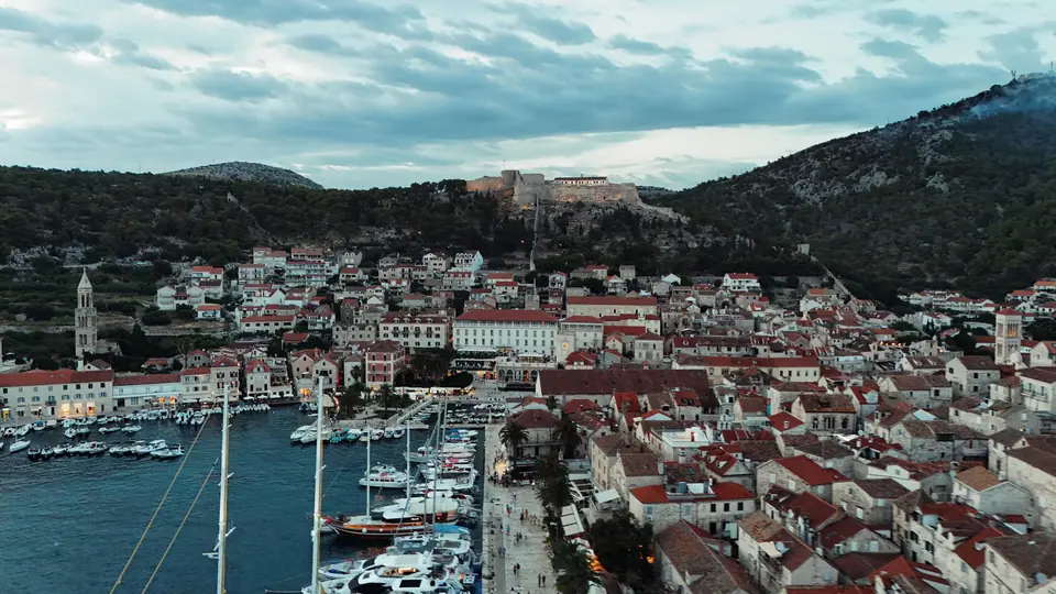 Wide drone view of Croatian harbor and stone town at dusk.