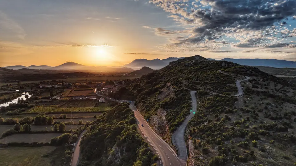 Sunset drone landscape with winding road and layered hills.