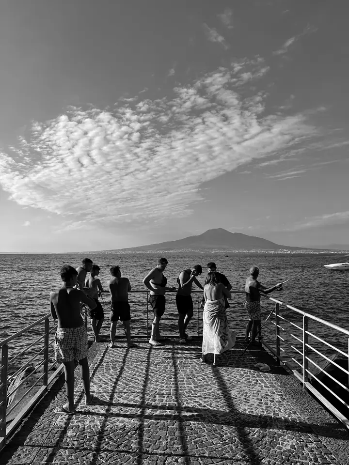 Pier scene in Naples with figures set against water and volcanic horizon.