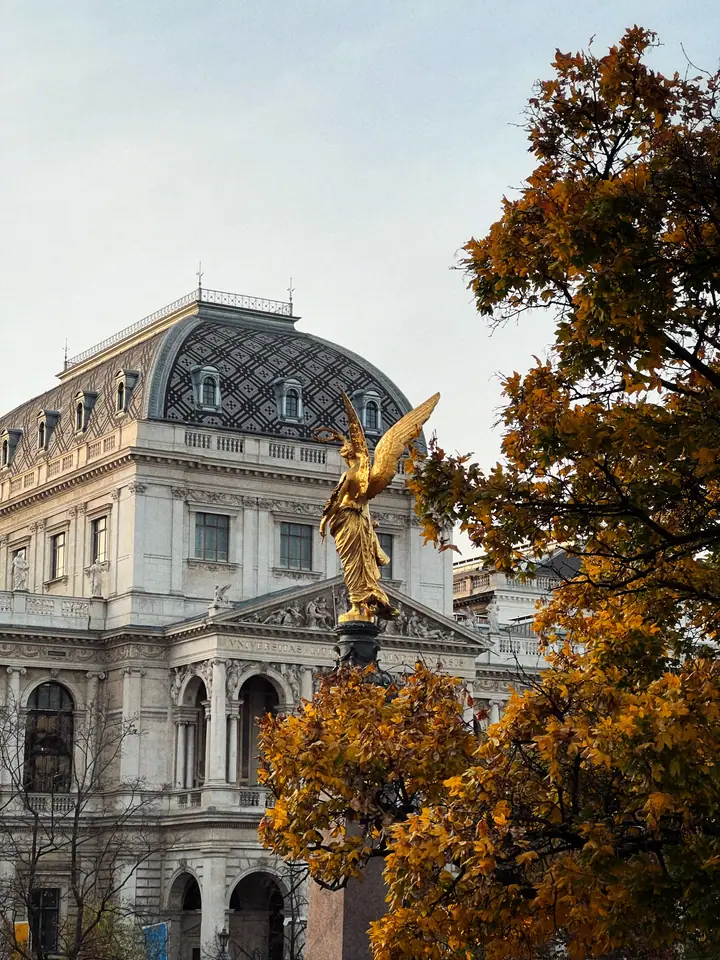 Golden monument framed by Vienna architecture and autumn foliage.